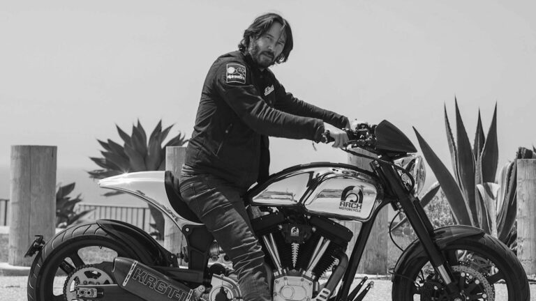 A man in a jacket mounts a sleek motorcycle beside large agave plants, in a grayscale setting, exuding a cool, adventurous vibe.